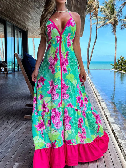 Woman wearing a floral halter-neck maxi dress with deep V-neckline and solid trim, standing by a tropical infinity pool
