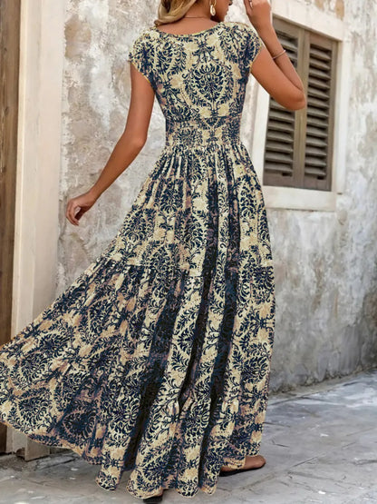 Woman wearing a maroon floral V-neck maxi dress with cap sleeves and high slit, styled with a straw hat and handbag in a tropical outdoor setting.