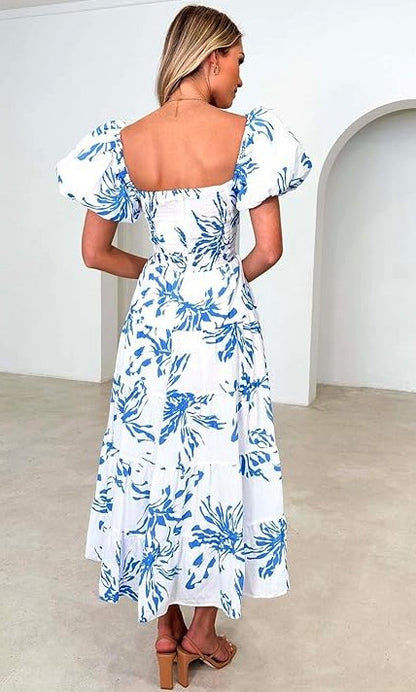 A white maxi dress with a blue botanical print features short puff sleeves and a wrap-style bodice that ties at the waist.