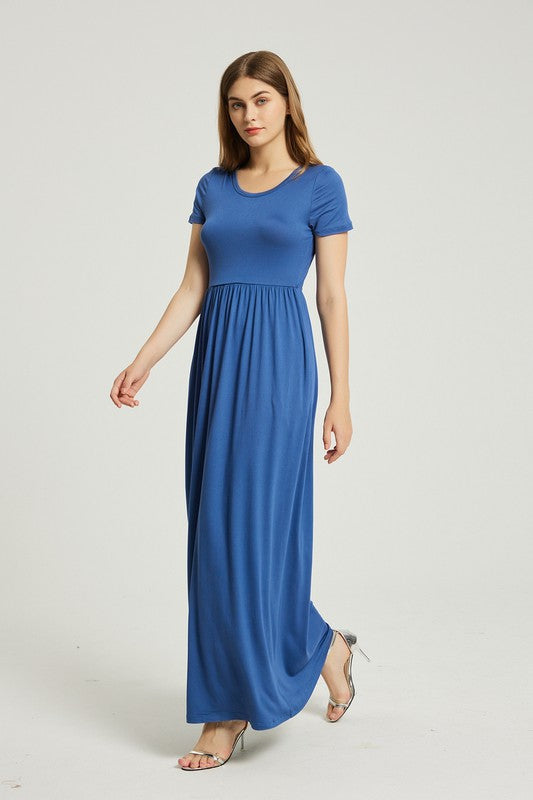 A woman in a blue dress sits on a wooden chair with a black backrest, posing against a plain background.