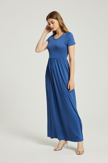 A woman in a blue dress sits on a wooden chair with a black backrest, posing against a plain background.