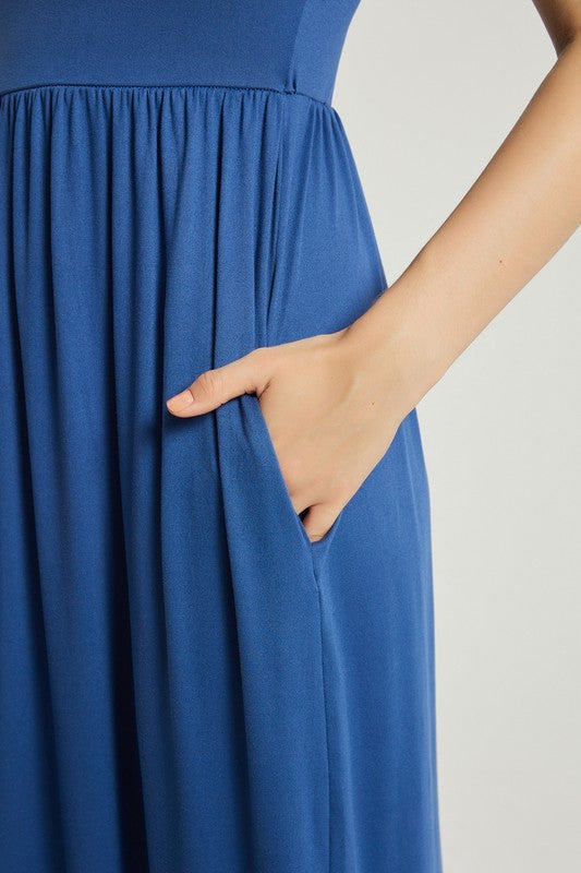 A woman in a blue dress sits on a wooden chair with a black backrest, posing against a plain background.
