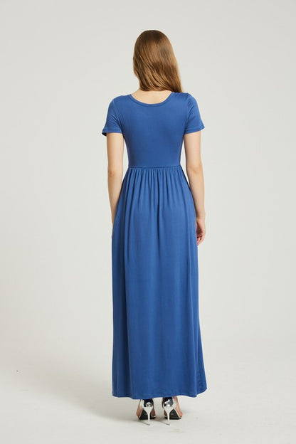 A woman in a blue dress sits on a wooden chair with a black backrest, posing against a plain background.
