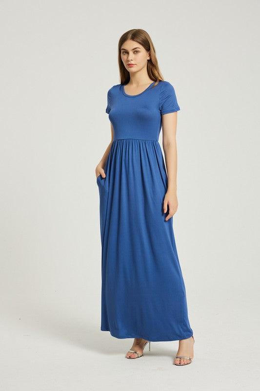 A woman in a blue dress sits on a wooden chair with a black backrest, posing against a plain background.