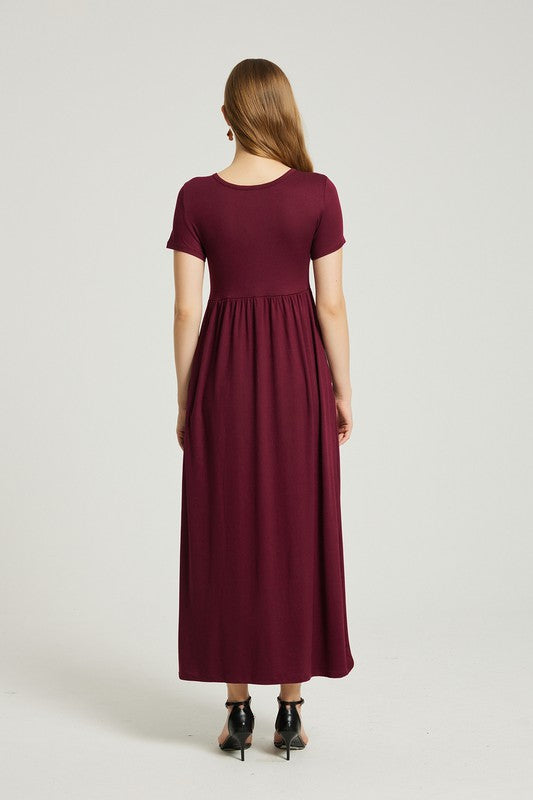 A woman in a maroon dress sits on a wooden chair with a black backrest, posing against a plain background.