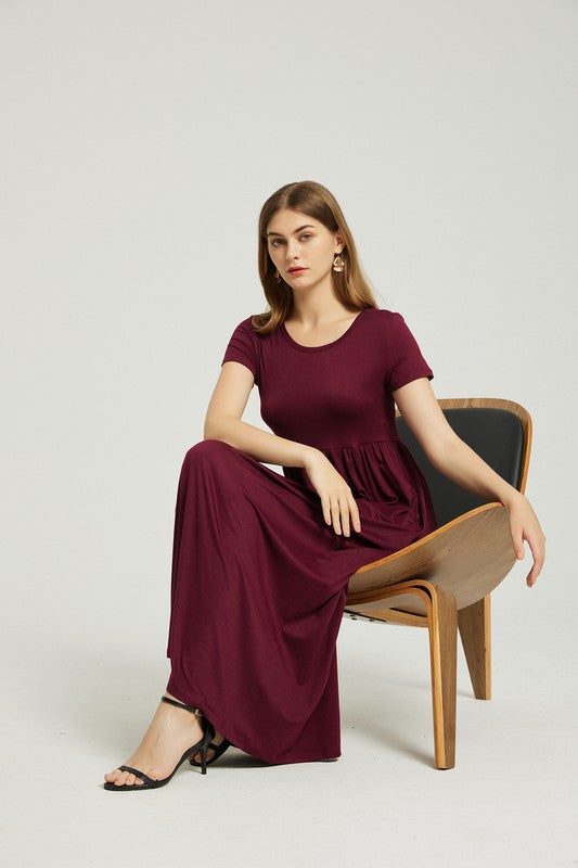 A woman in a maroon dress sits on a wooden chair with a black backrest, posing against a plain background.