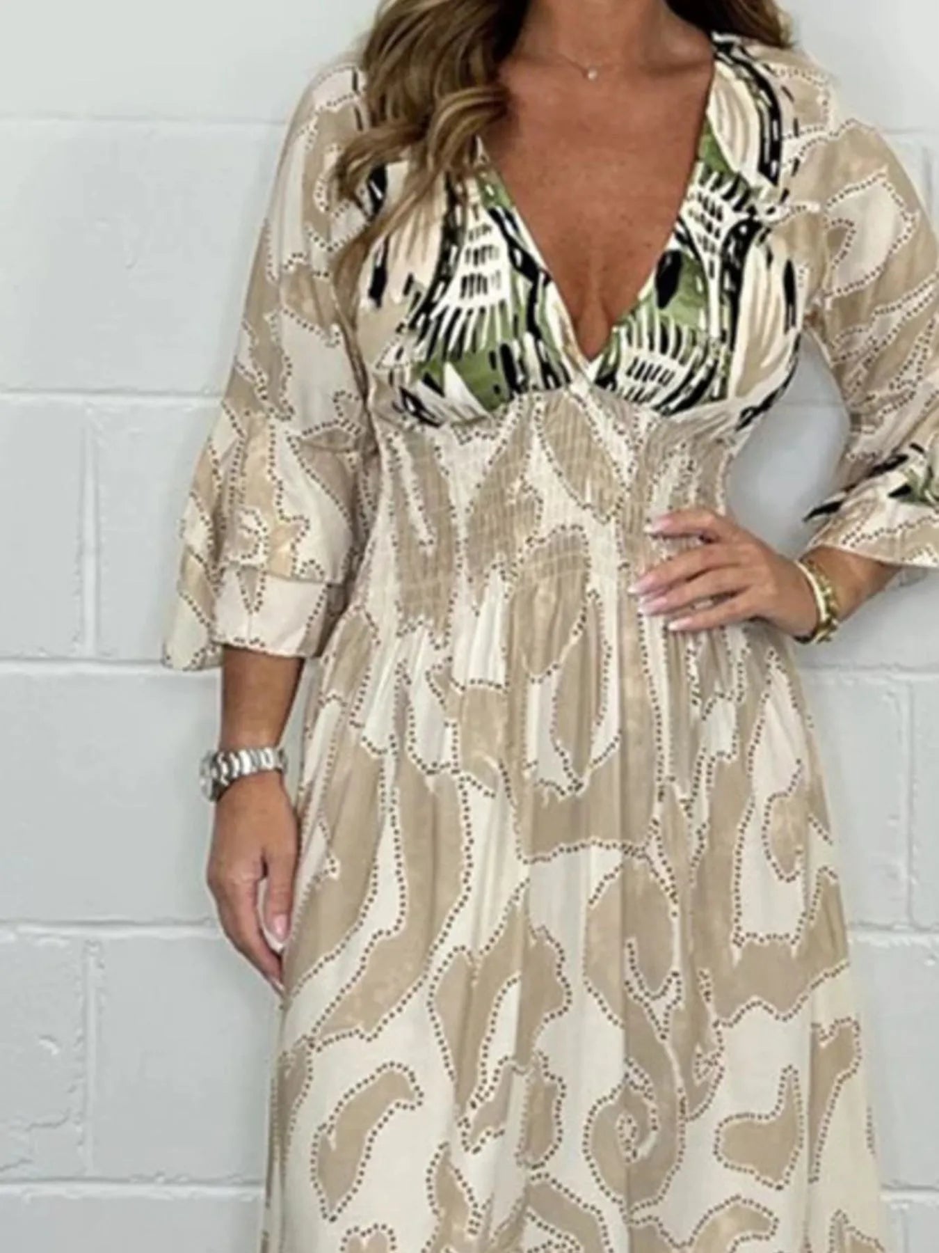 Woman wearing a full-length printed V-neck maxi dress with long flared sleeves and mixed abstract and animal patterns, styled with open-toe heels.