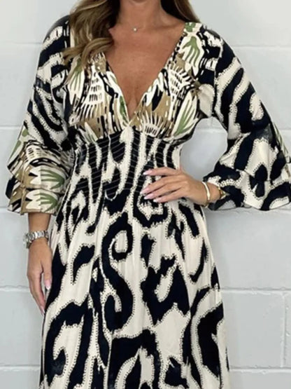 Woman wearing a full-length printed V-neck maxi dress with long flared sleeves and mixed abstract and animal patterns, styled with open-toe heels.