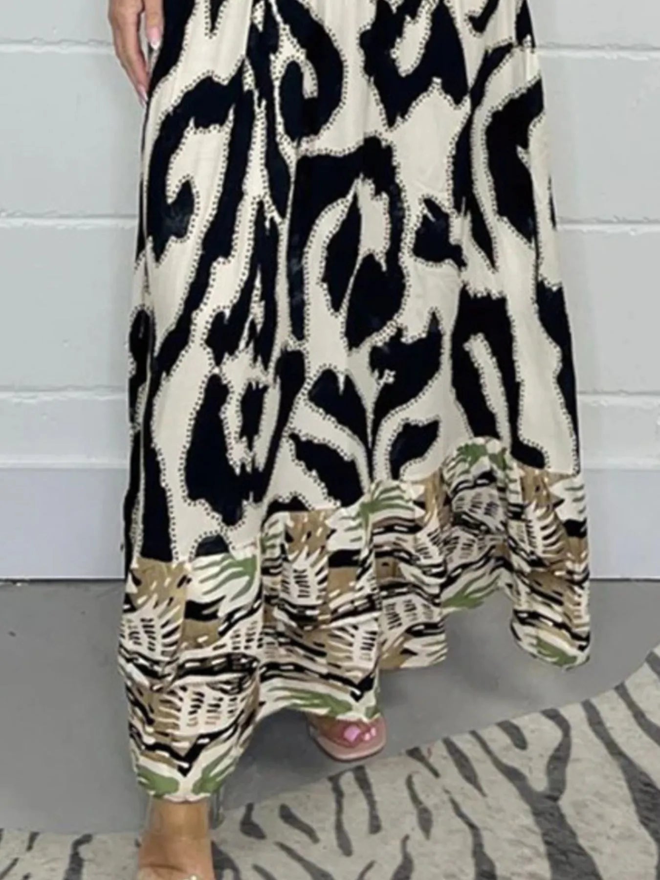 Woman wearing a full-length printed V-neck maxi dress with long flared sleeves and mixed abstract and animal patterns, styled with open-toe heels.