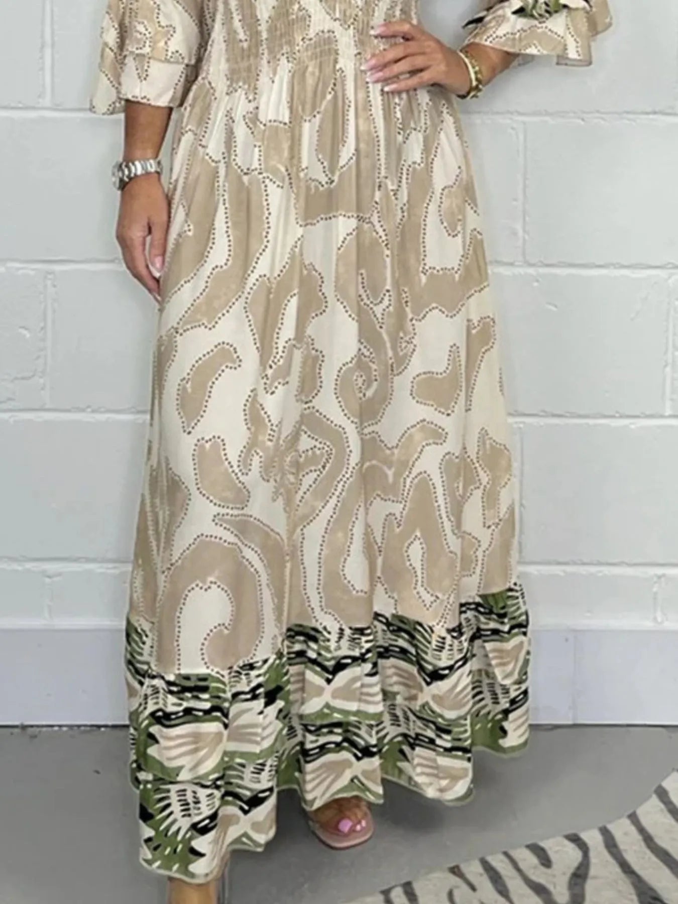 Woman wearing a full-length printed V-neck maxi dress with long flared sleeves and mixed abstract and animal patterns, styled with open-toe heels.