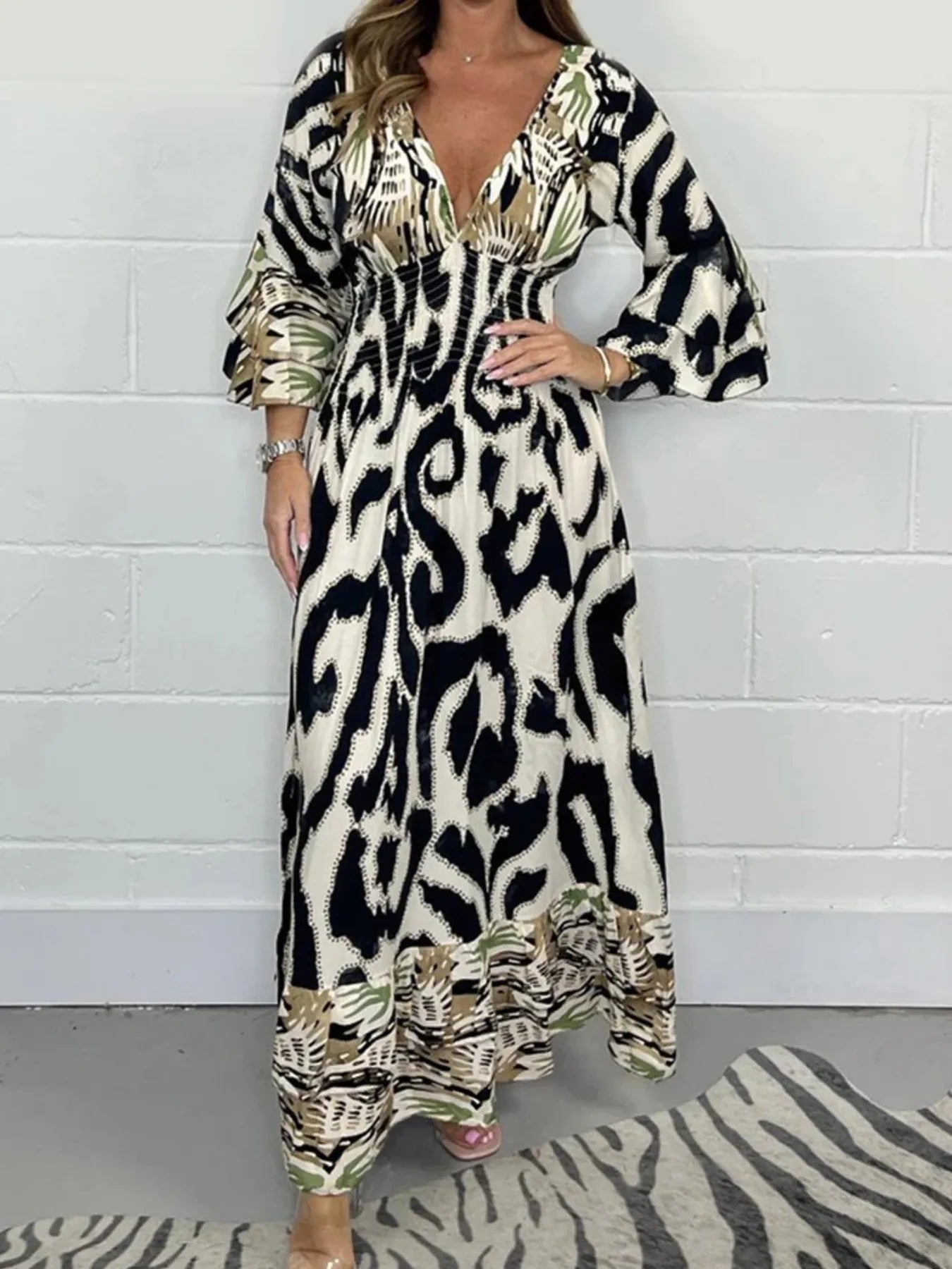 Woman wearing a full-length printed V-neck maxi dress with long flared sleeves and mixed abstract and animal patterns, styled with open-toe heels.