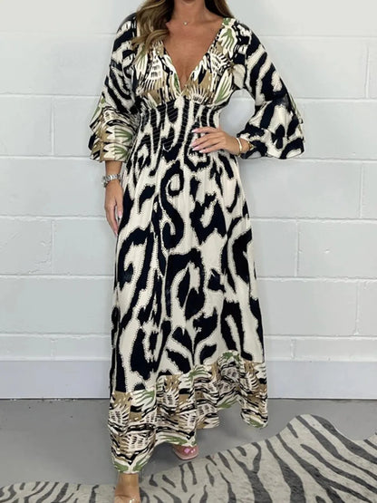 Woman wearing a full-length printed V-neck maxi dress with long flared sleeves and mixed abstract and animal patterns, styled with open-toe heels.