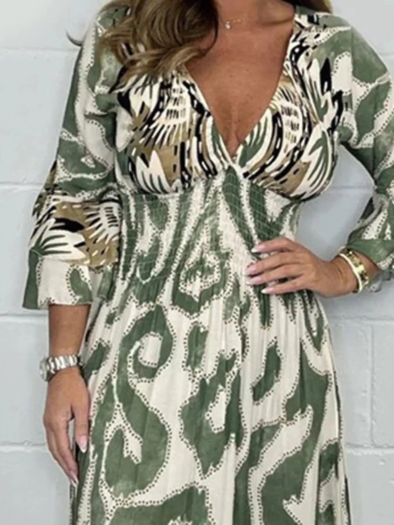 Woman wearing a full-length printed V-neck maxi dress with long flared sleeves and mixed abstract and animal patterns, styled with open-toe heels.