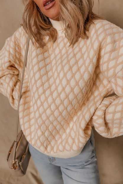 Woman wearing a beige and cream rhombus texture sweater with a mock neck and dropped shoulders, posing with hands on waist.