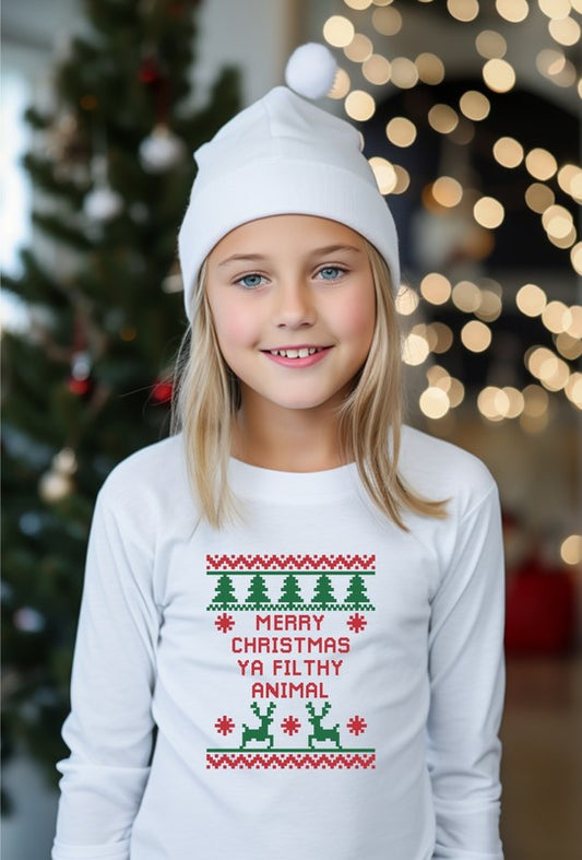 Child wearing a white long-sleeve shirt with Christmas-themed design in front of a decorated Christmas tree.